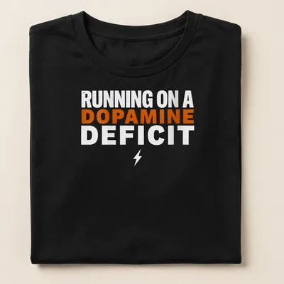 Bold typography humor t-shirt with the phrase 'RUNNING ON A DOPAMINE DEFICIT' in orange and white. — printed on a women's shirt